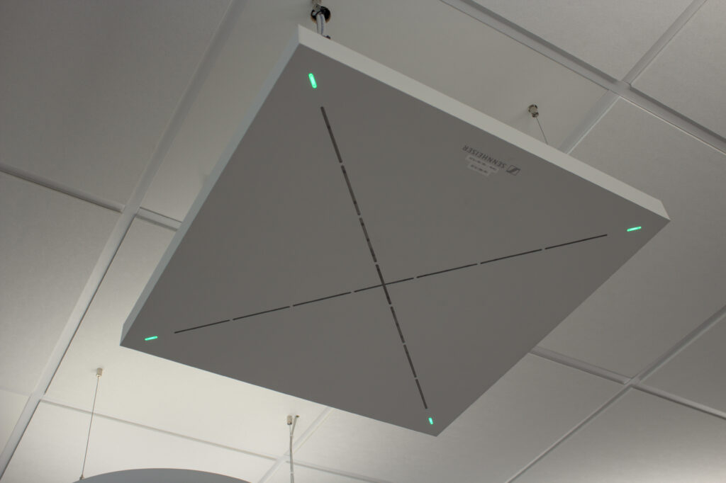 Ein weißes, quadratisches Mikrofon unter einer Rasterdecke